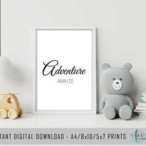 May include: A white framed print with black text that reads "Adventure Awaits". The print is sitting on a white surface with a gray teddy bear and a wooden toy helicopter.