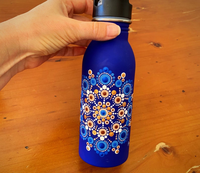 May include: A blue water bottle with a mandala design painted on it. The mandala is made up of blue, white, and gold dots.