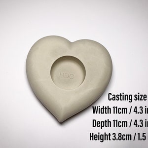 May include: A white heart-shaped mold for casting concrete or resin. The mold is 4.3 inches wide, 4.3 inches deep, and 1.5 inches tall. The mold has a circular opening in the center.