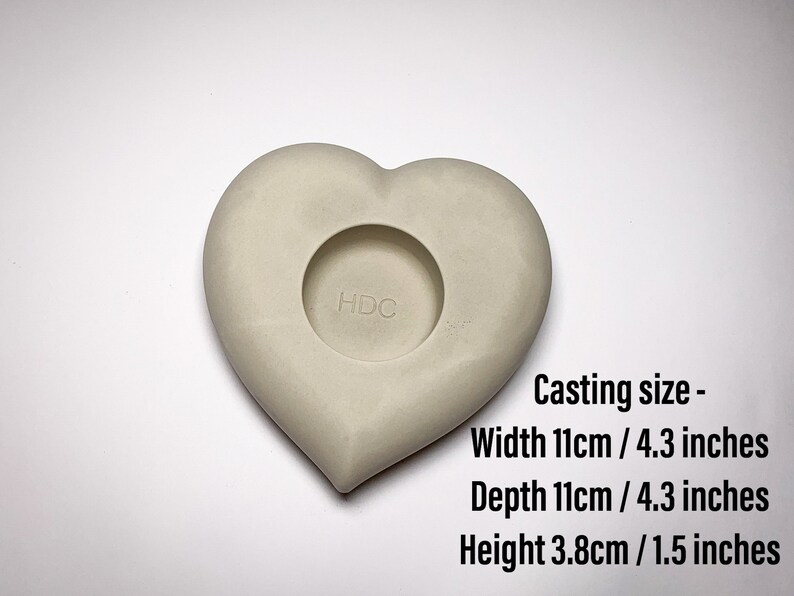 May include: A white heart-shaped mold for casting concrete or resin. The mold is 4.3 inches wide, 4.3 inches deep, and 1.5 inches tall. The mold has a circular opening in the center.