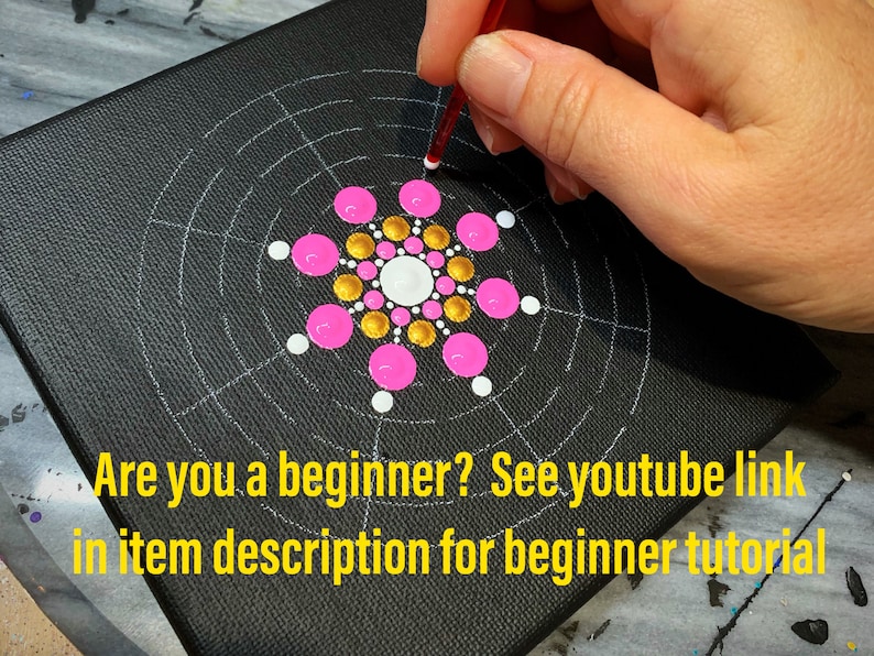 May include: A close-up of a black canvas with a white grid pattern. The center of the canvas features a pink and gold dot mandala design. A hand is holding a red tool and placing a white dot on the canvas. "Are you a beginner? See youtube link in item description for beginner tutorial" is written in yellow text at the bottom of the canvas.