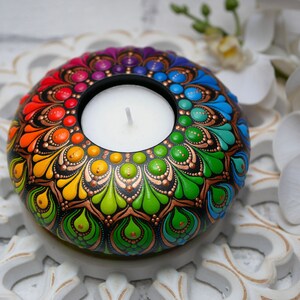 K&ouml;nnte beinhalten: Ein Teelichthalter mit einem Regenbogen-Mandala-Design, schwarzem Hintergrund und goldenen Akzenten. Der Halter hat ein kreisf&ouml;rmiges Design mit einer zentralen Vertiefung f&uuml;r ein Teelicht.