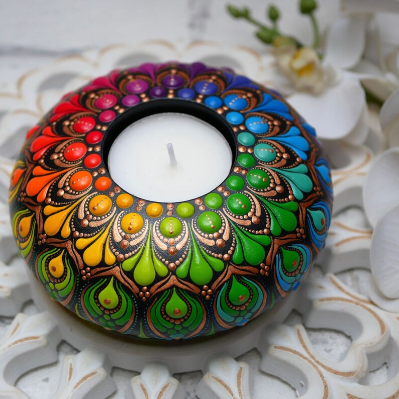 K&ouml;nnte beinhalten: Ein Teelichthalter mit einem Regenbogen-Mandala-Design, schwarzem Hintergrund und goldenen Akzenten. Der Halter hat ein kreisf&ouml;rmiges Design mit einer zentralen Vertiefung f&uuml;r ein Teelicht.