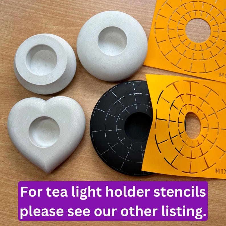 May include: Four concrete candle holders in different shapes: a round one, a heart-shaped one, and two round ones with a raised rim. The round candle holders are white, the heart-shaped one is gray, and the raised rim candle holders are white with a gray speckled finish. Two orange stencils with a circular design are also shown.
