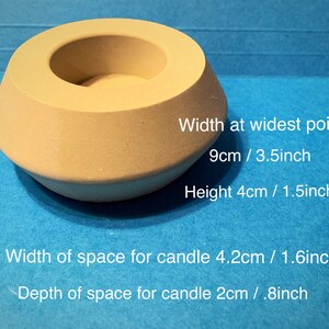 May include: A beige concrete candle holder with a wide opening and a smaller opening in the center. The holder is 3.5 inches wide and 1.5 inches tall. The space for the candle is 1.6 inches wide and 0.8 inches deep.
