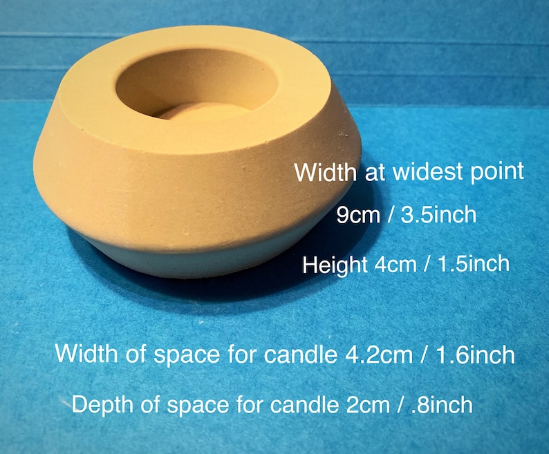 May include: A beige concrete candle holder with a wide opening and a smaller opening in the center. The holder is 3.5 inches wide and 1.5 inches tall. The space for the candle is 1.6 inches wide and 0.8 inches deep.