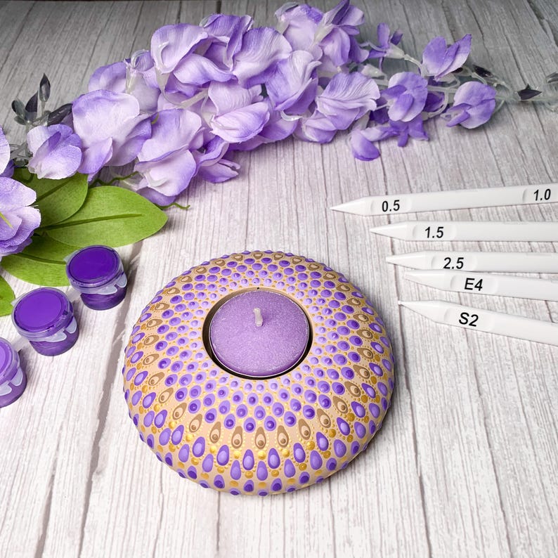 K&ouml;nnte beinhalten: Lilafarbener und goldener Mandala-Teelichthalter mit einem lilafarbenen Teelicht darin. Der Halter ist aus Holz und hat ein gepunktetes Muster. Es gibt vier kleine Gl&auml;ser mit lilafarbener Farbe und vier wei&szlig;e Punktwerkzeuge in den Gr&ouml;&szlig;en 0,5, 1,0, 1,5, 2,5, E4 und S2.