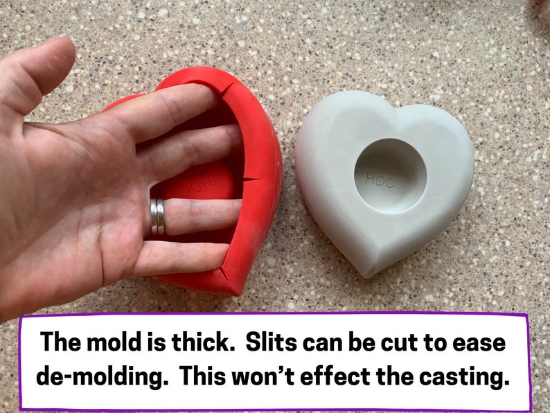 May include: Two heart-shaped silicone molds, one red and one gray. The red mold has slits cut into the side to make it easier to remove the finished product. The gray mold has a circular indentation in the center. The text "HDC" is printed on the gray mold.