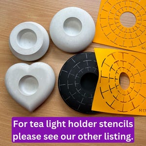 May include: Four concrete candle holders in different shapes: a round one, a heart-shaped one, and two round ones with a raised rim. The round candle holders are white, the heart-shaped one is gray, and the round ones with a raised rim are white. There are two orange stencils with a circular design, one black and one orange.