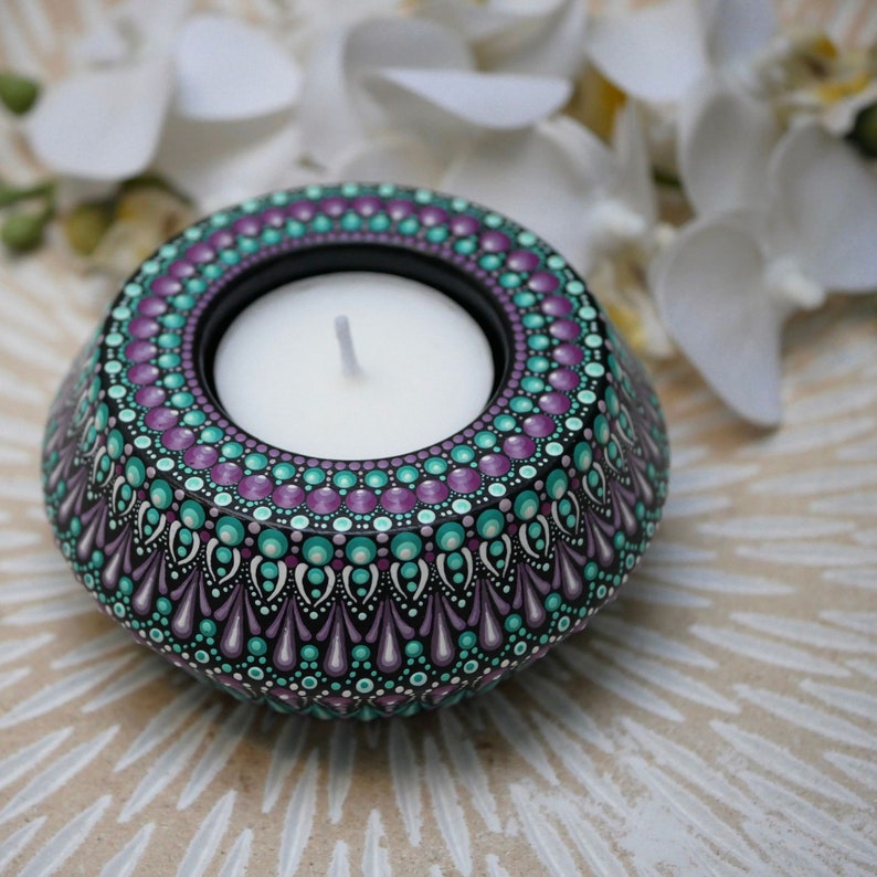 May include: Teal, purple, and white hand-painted tealight holder with a mandala design. The holder is made of wood and has a round shape.