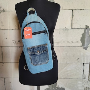 May include: A light blue denim crossbody bag with a zipper closure and a large front pocket. The bag has a black strap and a red tag that says "ONLY ONE".