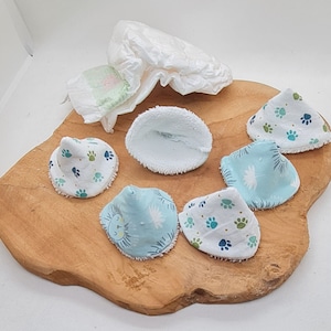 Peut inclure: Six disques démaquillants réutilisables, cinq avec un motif de pattes bleues et blanches et un avec un motif d'étoiles bleues et blanches. Les disques sont sur une surface en bois.