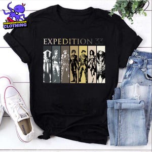 May include: Black t-shirt featuring the text "EXPEDITION 33" above a graphic of seven figures in a row. The figures are in various outfits and poses, with a color gradient background. The shirt has short sleeves and a crew neck.
