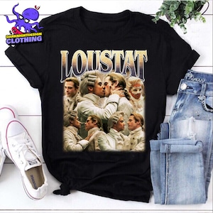 May include: Black t-shirt with a retro graphic design. The word "LOUSTAT" is displayed above a collage of historical figures in period attire, some in an embrace. The shirt is shown with blue jeans and white trainers.