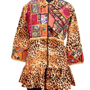 Puede incluir: Una chaqueta de estampado de leopardo marrón y negro con cierre de cremallera y detalles bordados de colores. La chaqueta tiene un dobladillo con volantes y mangas largas.