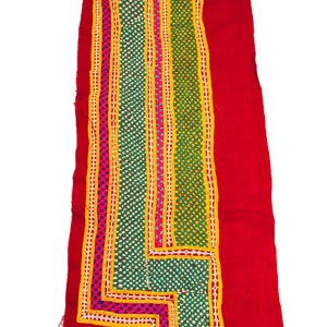Könnte beinhalten: Ein rotes Stoffpanel mit einem dekorativen Rand aus grüner, gelber, rosa und blauer Stickerei. Die Stickerei ist in einem geometrischen Muster.