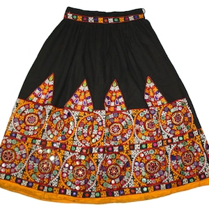 Peut inclure: Une jupe noire avec un motif brodé coloré. La jupe a une large ceinture et une silhouette évasée. La broderie présente des motifs géométriques, des miroirs et des perles.