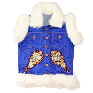 Könnte beinhalten: Eine blaue Jeansweste mit einem weißen Kunstfellkragen und Besatz. Die Weste hat zwei Taschen und einen Knopfverschluss. Die Weste ist mit goldenen und silbernen Verzierungen verziert.