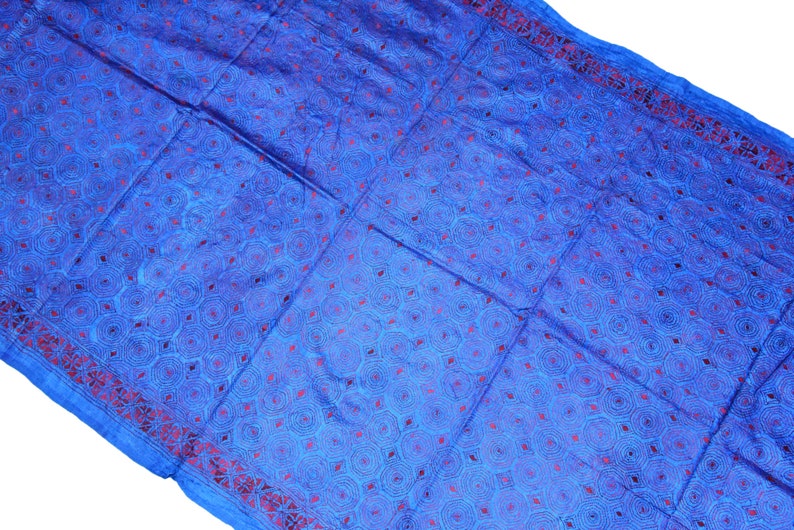May include: A blue fabric with a red and blue patterned design. The fabric has a geometric pattern of circles and diamonds.