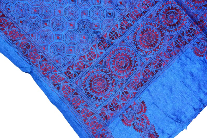 May include: A blue silk scarf with a burgundy embroidered border featuring intricate geometric patterns. The design includes circles, squares, and triangles.
