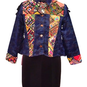 Könnte beinhalten: Eine blaue Jeansjacke mit Tarnmuster und bunten Stickereien. Die Jacke hat einen Knopfschließe vorne und lange Ärmel.
