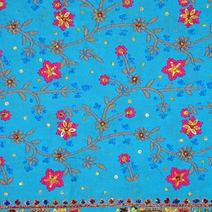 May include: A turquoise fabric with a floral pattern embroidered with pink, yellow, and blue thread. The fabric has a gold and silver trim with colorful jewels.