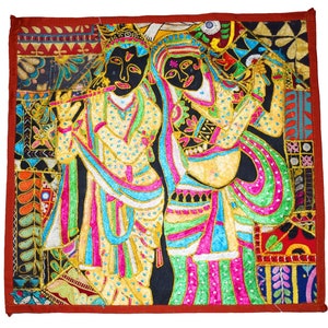 May include: A colorful embroidered wall hanging featuring a couple in traditional Indian clothing. The woman is playing a musical instrument, while the man is holding a flute. The background is a patchwork of different fabrics and colors.