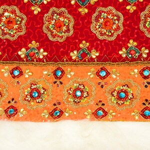 May include: A close-up of a red and orange fabric with intricate embroidery. The fabric has a beaded border and a white fur trim.