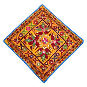 Puede incluir: Un cojín cuadrado con fondo amarillo y un patrón floral colorido. El cojín está bordado con espejos y tiene un borde azul.