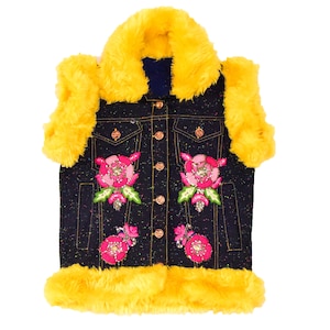 Könnte beinhalten: Eine ärmellose Jeansweste mit einem gelben Kunstfellkragen und Besatz. Die Weste hat einen Knopfverschluss und ist mit rosa und grünen Blumenstickereien verziert.