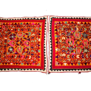 Könnte beinhalten: Zwei quadratische bestickte Wandbehänge mit komplizierten floralen und geometrischen Mustern in Rot-, Orange-, Gelb-, Rosa-, Blau- und Grüntönen. Die Wandbehänge haben kleine runde Spiegel und Quasten.