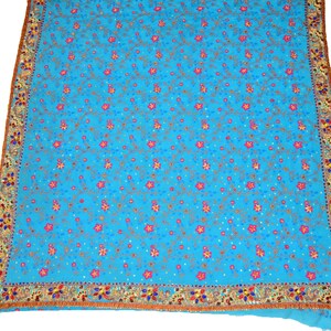 May include: A turquoise blue fabric with a floral pattern embroidered with pink, gold, and blue thread. The fabric has a gold and red border with sequins.