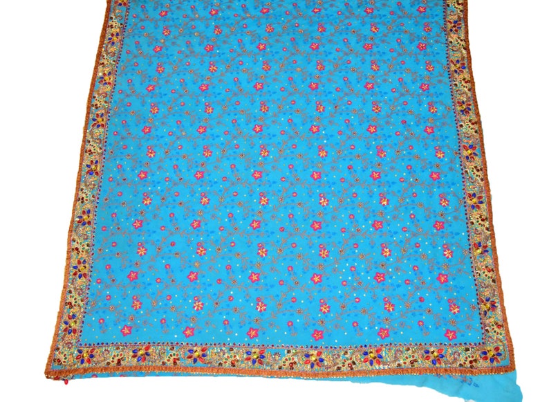 May include: A turquoise blue fabric with a floral pattern embroidered with pink, gold, and blue thread. The fabric has a gold and red border with sequins.