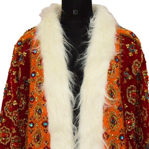 May include: A red and orange velvet jacket with a white fur collar. The jacket is heavily embellished with gold and jewel-toned sequins and beads.
