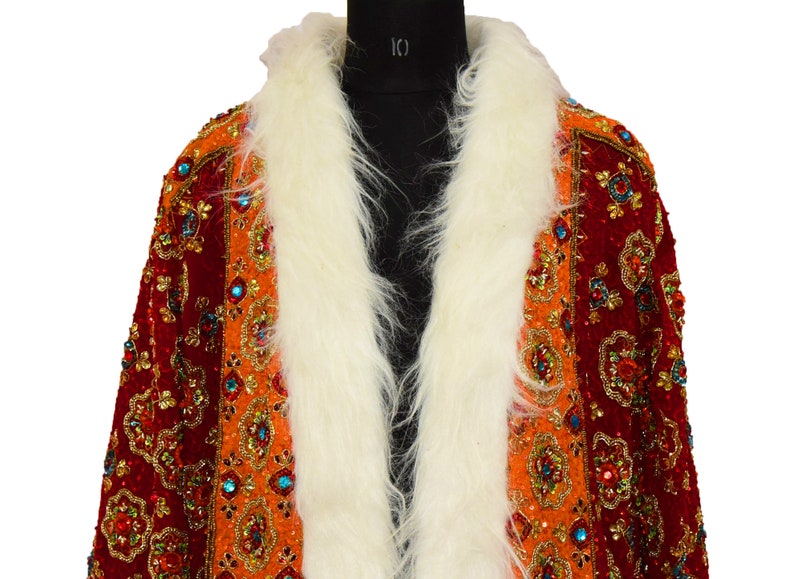 May include: A red and orange velvet jacket with a white fur collar. The jacket is heavily embellished with gold and jewel-toned sequins and beads.
