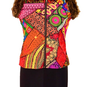 May include: A sleeveless vest with a brown faux fur collar and a zipper closure. The vest is made of a patchwork of colorful fabrics with intricate embroidery and sequins.