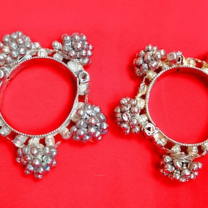 Può includere: Due braccialetti d'argento con decorazioni rotonde decorative. I braccialetti sono in metallo e hanno una finitura lucida.