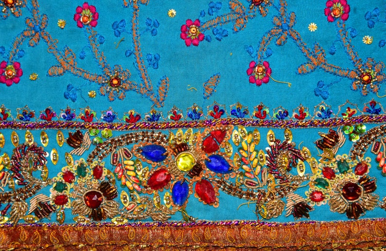 May include: A turquoise fabric with intricate embroidery and beaded embellishments. The design features floral motifs and a border of sequins and beads.