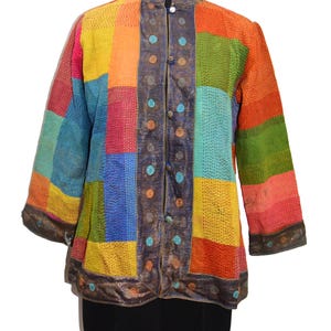 Könnte beinhalten: Eine langärmelige Jacke mit einem Patchwork-Design aus rechteckigen Feldern in leuchtendem Gelb, Orange, Grün, Blau und Pink. Das Kleidungsstück hat einen dunkelblauen Besatz entlang der Vorderöffnung, des Kragens und der Ärmelbündchen.