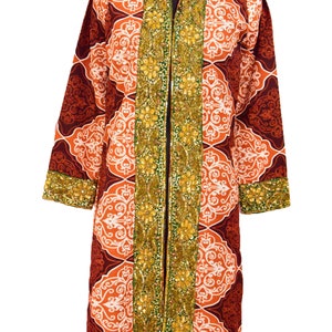 Könnte beinhalten: Ein langer, brauner und orangefarbener Mantel mit goldenen und grünen Perlenbesatz. Der Mantel hat einen Stehkragen und einen Reißverschluss vorne.