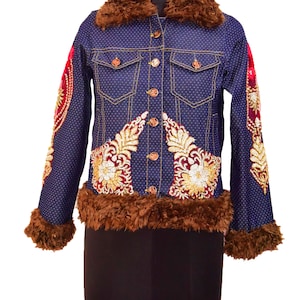 Könnte beinhalten: Eine blaue Jeansjacke mit weißen Punkten und goldenen und roten Stickereien. Die Jacke hat einen braunen Kunstfellkragen und -ärmel.