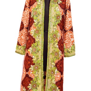 Könnte beinhalten: Eine lange, rot-orange-weiß gemusterte Robe mit grüner und goldener Perlenbesatz. Die Robe hat einen Kragen und lange Ärmel.
