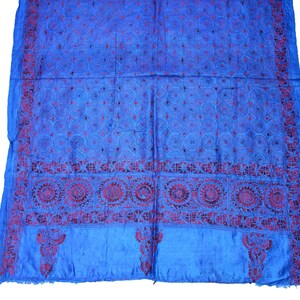 May include: A blue silk scarf with intricate red embroidery. The embroidery features a repeating geometric pattern and a border of floral motifs.