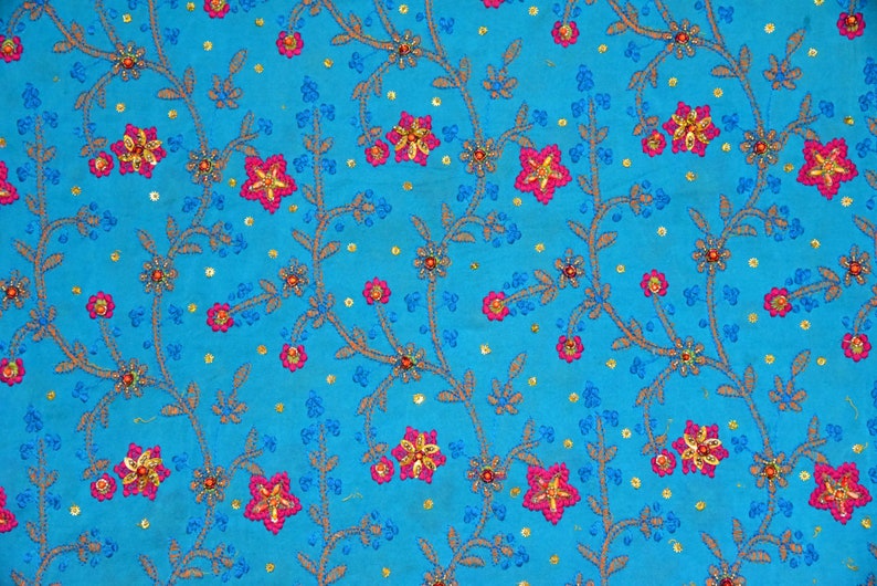 May include: A blue fabric with a floral pattern embroidered with pink and gold flowers. The fabric is covered in small gold and blue sequins.