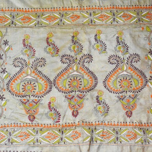 Könnte beinhalten: Ein beigefarbener Stoff mit aufwendigen Stickereien in Grün-, Orange- und Brauntönen. Das Design zeigt sich mit sich wiederholenden floralen Motiven und Paisley-Mustern.