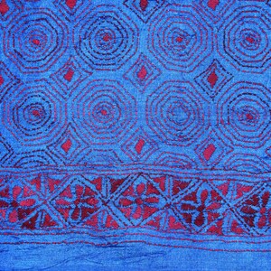May include: Blue fabric with a red embroidered pattern of circles and diamonds. The fabric has a textured surface.
