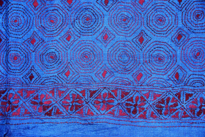 May include: Blue fabric with a red embroidered pattern of circles and diamonds. The fabric has a textured surface.