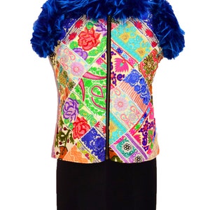 Könnte beinhalten: Eine bunte Patchwork-Weste mit einer lebendigen Auswahl an gestickten Blumen- und Paisley-Designs. Die Weste hat einen schwarzen Reißverschluss und ist mit einem flauschigen, königsblauen Federkragen versehen. Das Kleidungsstück wird auf einer Schaufensterpuppe präsentiert.