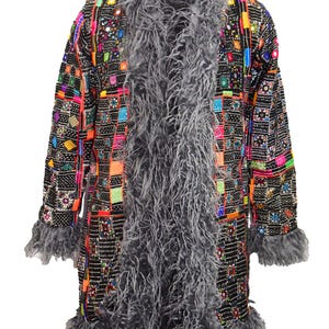Könnte beinhalten: Eine lange, schwarze Jacke mit einem bunten geometrischen Muster und einem grauen Kunstpelzbesatz. Die Jacke hat einen Schalkragen und lange Ärmel.