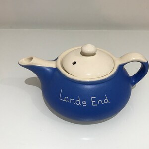 May include: A blue ceramic teapot with a white lid and the words "Lands End" written on the side.